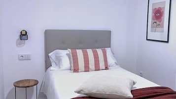 Un dormitorio ordenado con cama, almohadas, mesita de noche y una lámpara de pared.