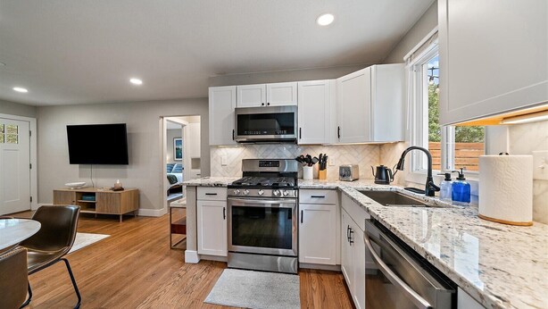 A modern kitchen with white cabinets, a built-in microwave, stainless steel appliances, and a granite countertop.