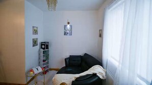A living room with a black sofa, a white throw blanket, a hanging light fixture, and a small wall-mounted picture. - Wythenshawe Greenbrow Retreat (Manchester)