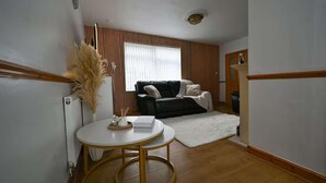 A living room with a black sofa, a white round table with a gold base, and a white rug. - Wythenshawe Greenbrow Retreat (Manchester)
