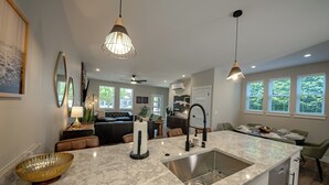 A modern kitchen with a marble countertop, stainless steel sink, and pendant lighting.