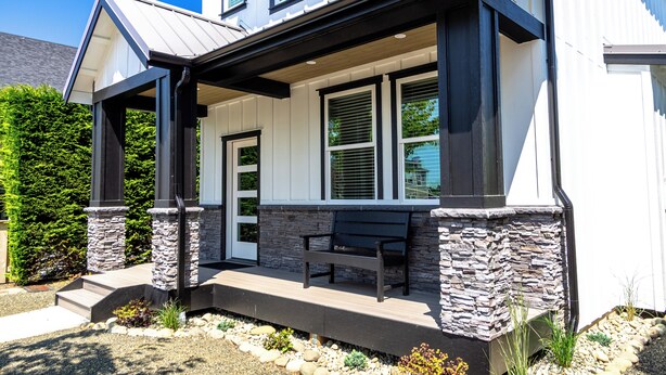 A modern two-story house with a covered porch, stone pillars, and a bench.