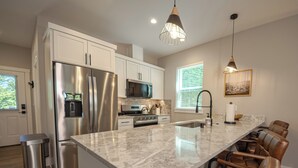 A modern kitchen with stainless steel appliances, a marble countertop, and a bar area with leather chairs.