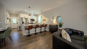 A modern kitchen with a central island, bar stools, and a dining area with a green chair.