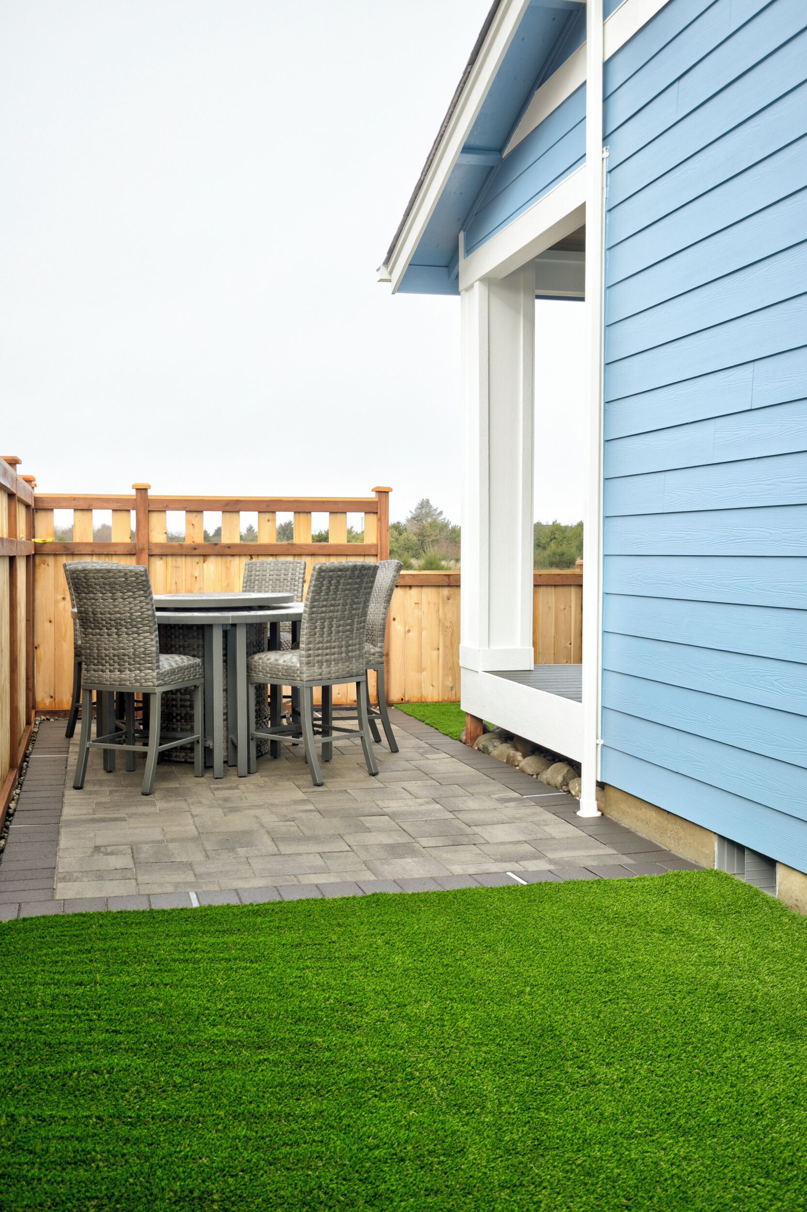 Une terrasse avec une table et des chaises, une clôture en bois et une maison bleue.