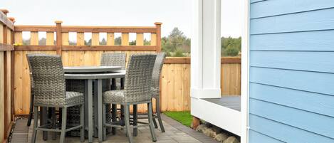 Une terrasse avec une table et des chaises, une clôture en bois et une maison bleue.
