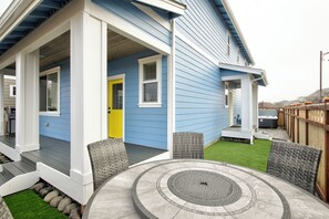 Une maison bleue avec un porche, une porte jaune et une terrasse dotée d’un foyer circulaire.