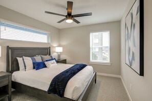 Une chambre à coucher avec un lit, une table de chevet, un ventilateur de plafond et deux fenêtres.