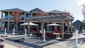 Ein Sitzbereich im Freien mit Tischen und Stühlen, eine überdachte Terrasse und im Hintergrund ein Gebäude mit dem Schild "The Grill".