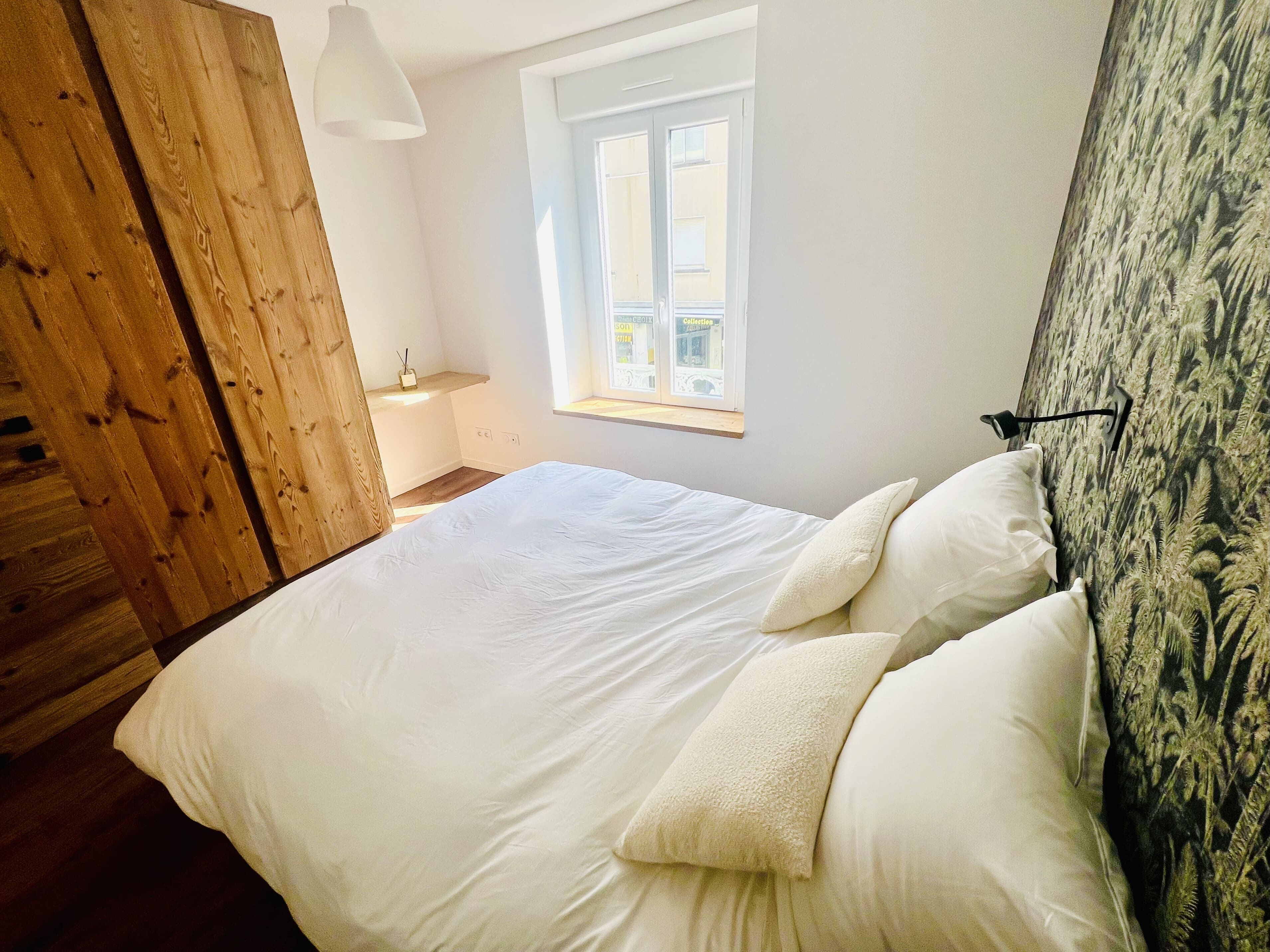 A bedroom with a large bed, a wooden wardrobe, a window with a view, and a wall with a textured pattern.