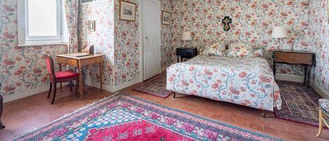 Een slaapkamer met bloemenbehang, een bed, een bureau en een stoel.