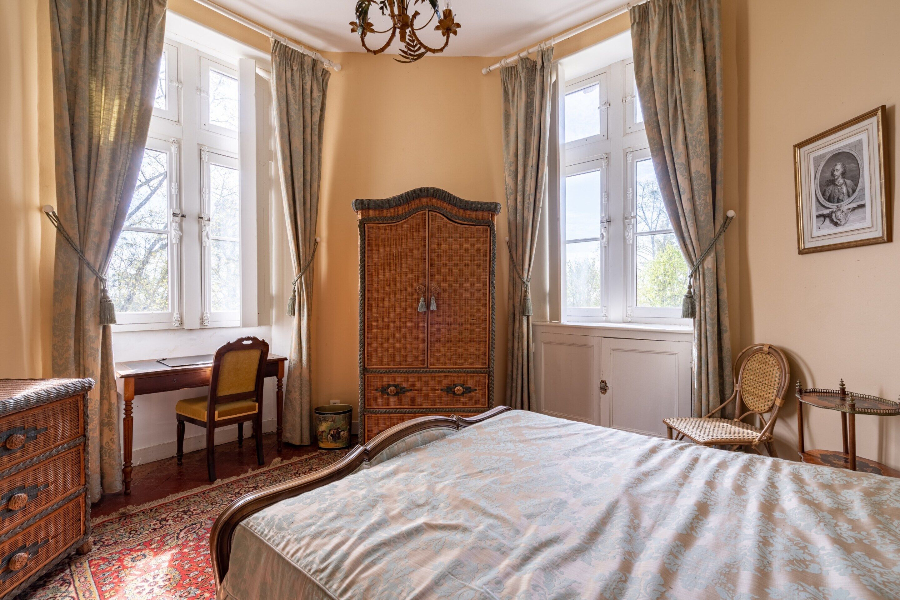 Un dormitorio con una cama grande, un armario de madera, un escritorio con una silla y una ventana con cortinas.
