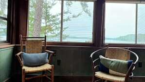 Two wicker chairs with cushions, positioned near large windows with a view of trees and a lake. - Bay of the Moon at Wolf Point - Pet Friendly! (Crane Lake)
