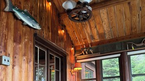 A cozy cabin interior with a wooden bed, a rustic ceiling, and a window overlooking greenery. - Bay of the Moon at Wolf Point - Pet Friendly! (Crane Lake)