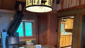 A wooden interior with a dining table, chairs, a wood stove, and a kitchen area. - Bay of the Moon at Wolf Point - Pet Friendly! (Crane Lake)