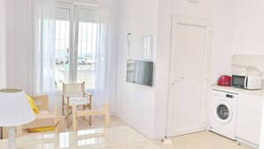 A compact living space with a dining table, chairs, a washing machine, and a microwave.