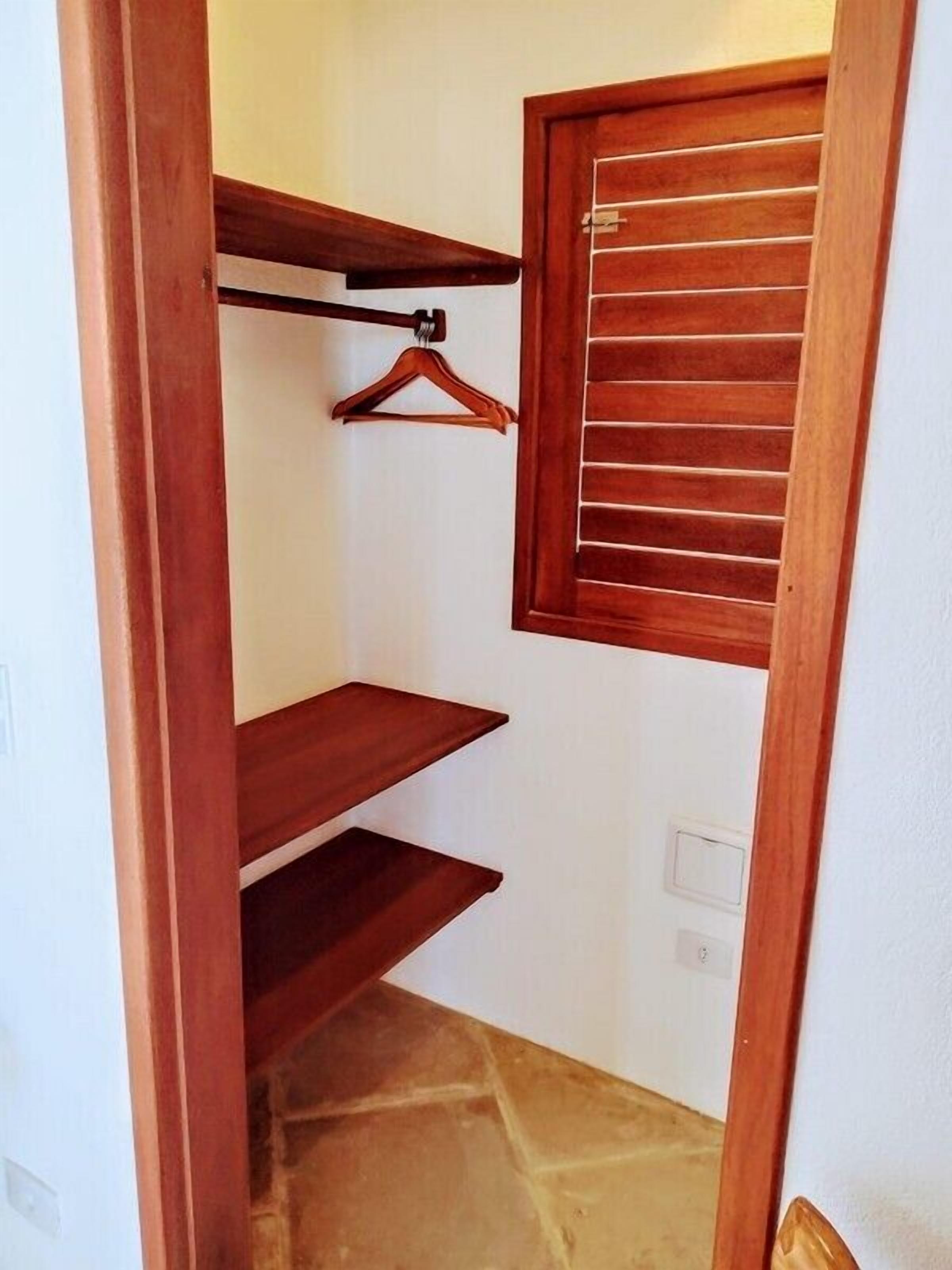 A wooden closet with three shelves and a window with blinds.
