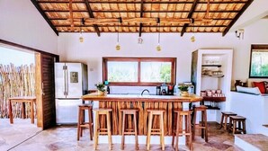 A kitchen with a central island, wooden stools, a refrigerator, and a window with a view. - Villa Pinolo (Cruz)