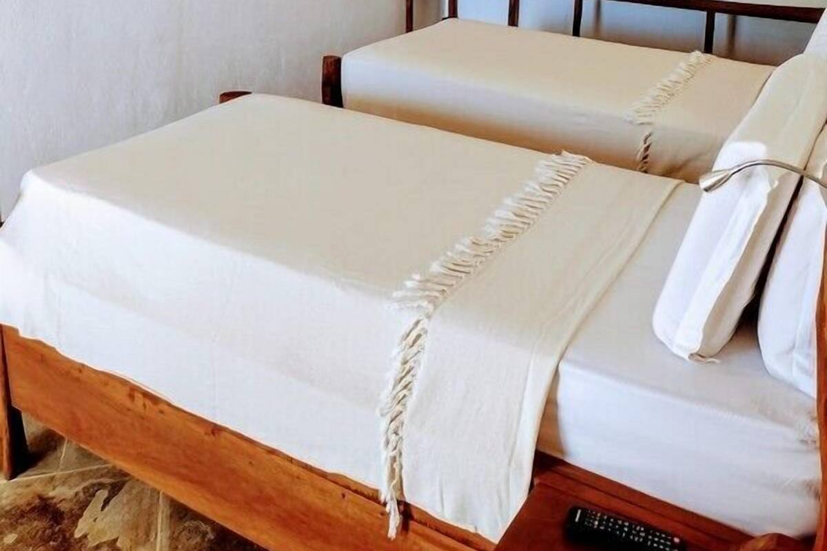Une chambre avec deux lits, un téléviseur fixé au mur, une étagère en bois et un appareil de climatisation.