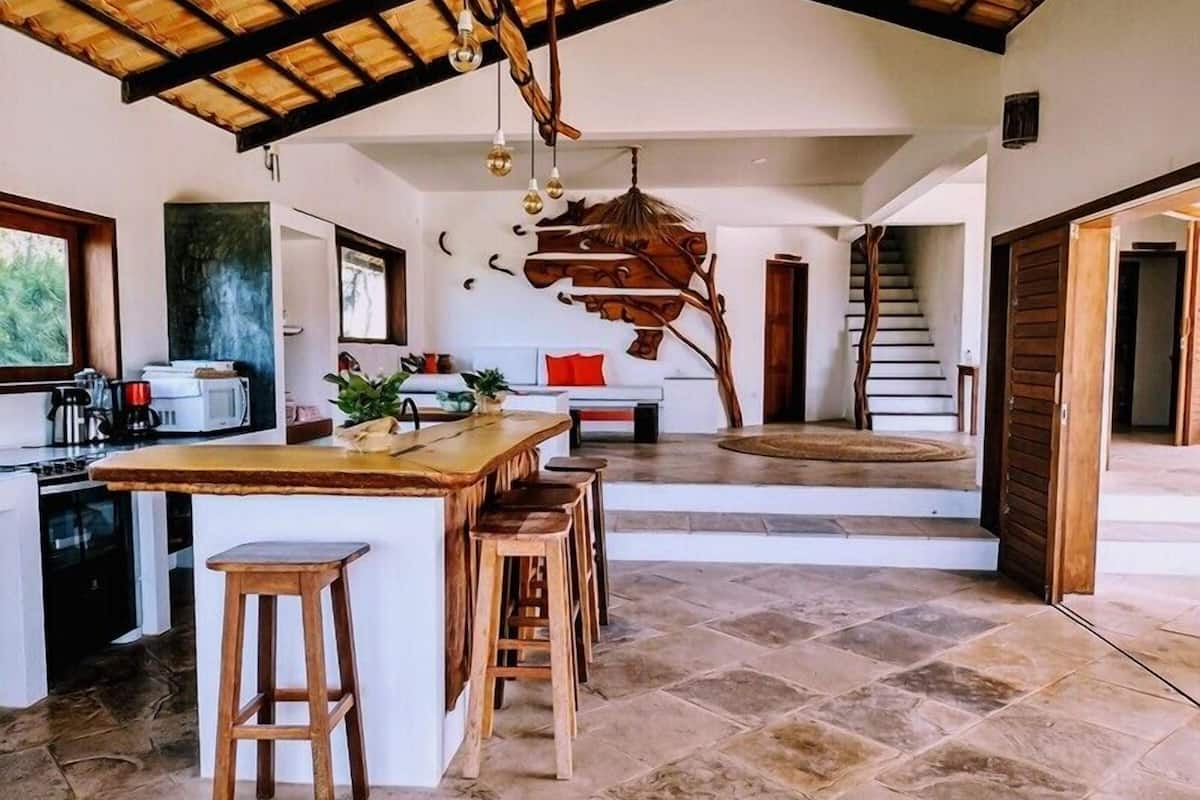 Une cuisine spacieuse avec un grand îlot central, des tabourets en bois et un plafond au style rustique.