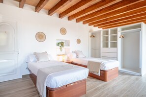 Une chambre avec deux lits, des poutres en bois, des murs blancs et un placard.