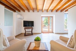 Un salon avec des poutres en bois, un téléviseur posé sur un meuble, deux canapés et une plante en pot.