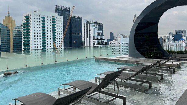 A rooftop pool with lounge chairs, a modern glass structure, and a city skyline in the background.