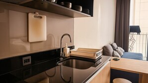 A modern kitchen with a black countertop, stainless steel sink, and a wooden dining area with a bar stool.