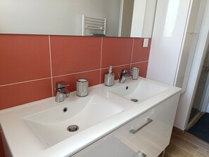 Une salle de bain moderne avec un lavabo blanc, deux robinets et un miroir au-dessus.