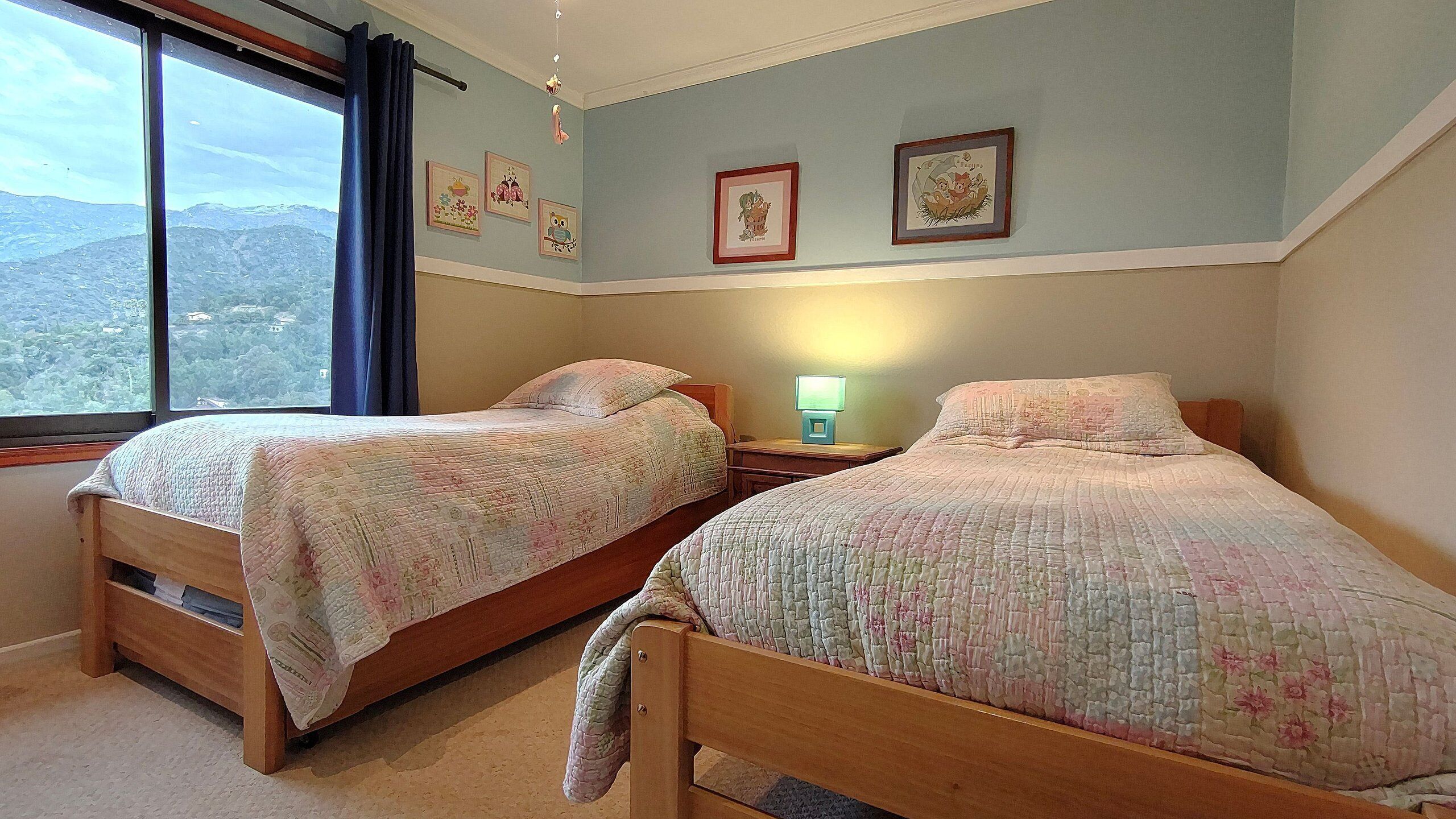 Una camera da letto con due letti in legno, un comodino con lampada e una finestra vista montagna.