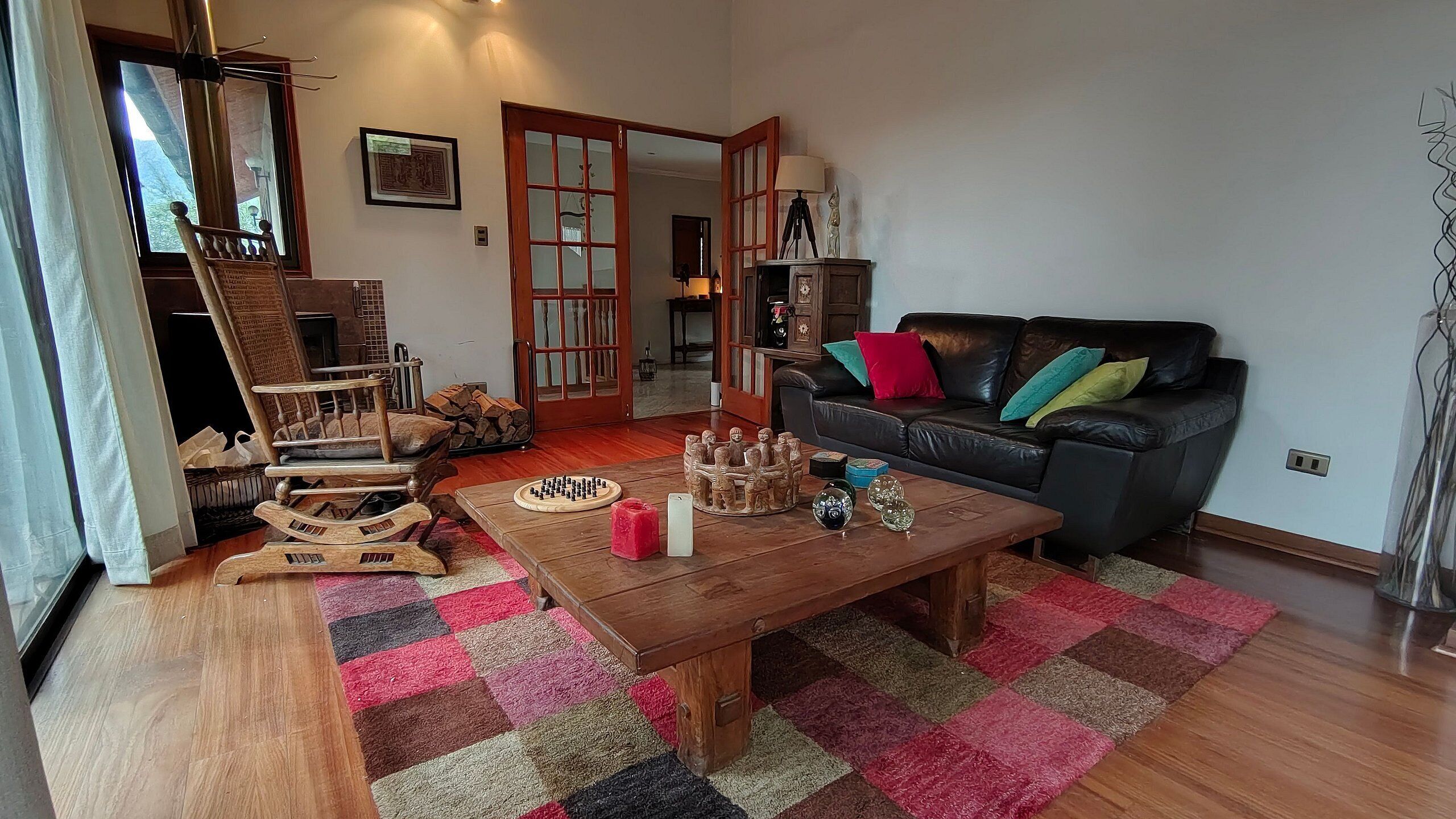 Un salón acogedor con una mesa de centro de madera, un sofá de cuero negro y una alfombra colorida.