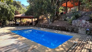 A swimming pool with a wooden deck, a covered seating area, and a stone wall. - Oceana Suites - Laguna Aculeo (Paine)