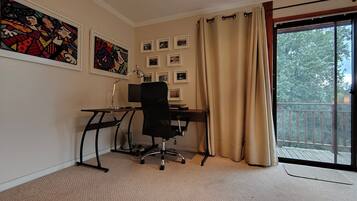 Een kamer met een bureau, stoel, computer en uitzicht op het groen via een schuifdeur.