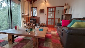 A cozy living room with a wooden table, a leather sofa, and a view of the outdoors. - Oceana Suites - Laguna Aculeo (Paine)