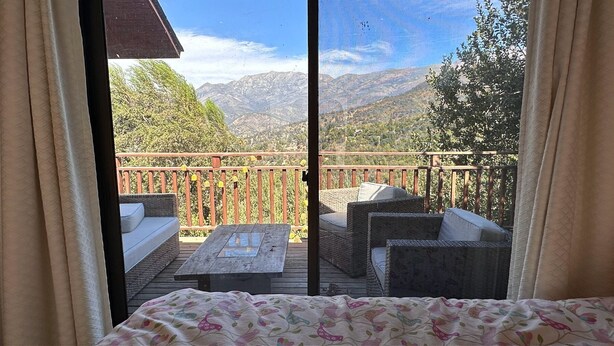 A balcony with wicker furniture, a wooden table, and a view of mountains. - Oceana Suites - Laguna Aculeo (Paine)