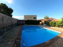 A swimming pool with a tiled deck, a metal ladder, and a stone wall on one side.