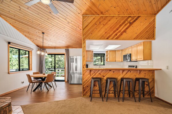 A modern kitchen with wooden cabinetry, a central island with stools, and a dining area with a table and chairs.
