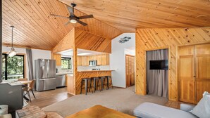 Un amplio salón con techo de madera, una cocina con barra y una zona de estar con sofá y mesa de centro.