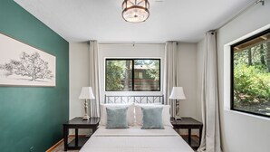 Un dormitorio con una cama grande, dos mesitas de noche, un ventanal con cortinas y vistas a zonas verdes.