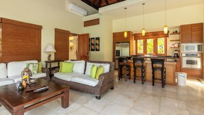 A modern living room with a sofa, coffee table, and kitchen area with bar stools. - Green Village 2BDR villa w/ pool (La Altagracia)