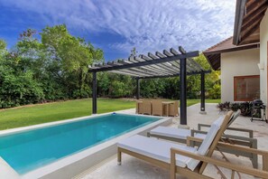 Une piscine rectangulaire, agrémentée de chaises longues et d’une pergola, située dans un jardin.