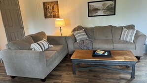 Un salon avec deux canapés gris, une table basse en bois, une lampe et une œuvre d’art encadrée accrochée au mur.