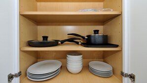 Une cuisine avec des étagères en bois, une poêle noire, une casserole noire et des assiettes blanches empilées.