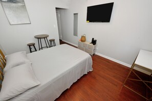 A room with a bed, a TV, a small table, stools, and a dresser. - Cozy Studio Near Central Park (New York)