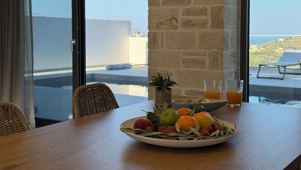 A dining table with a fruit bowl, a glass of orange juice, and a potted plant. - Sunrise Village Aptera Private Pool Villa No2 - Helios (Chania)