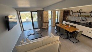 A modern kitchen with a dining area, a sofa, and a TV mounted on the wall. - Sunrise Village Aptera Private Pool Villa No2 - Helios (Chania)
