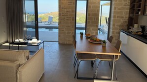 A modern kitchen with a dining area, large windows, and a view of the outdoors. - Sunrise Village Aptera Private Pool Villa No2 - Helios (Chania)