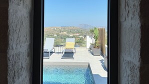 A view from inside a room to an outdoor swimming pool with a clear sky and distant landscape. - Sunrise Village Aptera Private Pool Villa No2 - Helios (Chania)