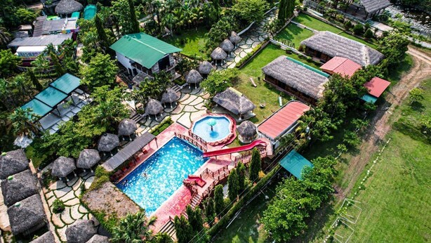 Vista aérea de un complejo turístico con piscina, cabañas de techo de paja y tobogán de agua.
