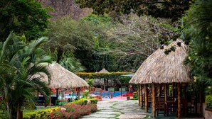 Un resort tropical con estructuras de techo de paja, piscina y exuberante vegetación.